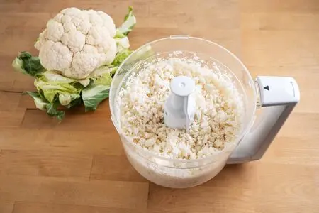 Un chou-fleur et du chou-fleur râpé dans un robot culinaire
