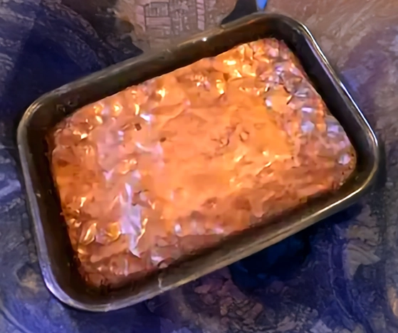 Brownie maison au chocolat, encore dans son moule métallique rectangulaire, surface brillante et craquelée caractéristique après cuisson