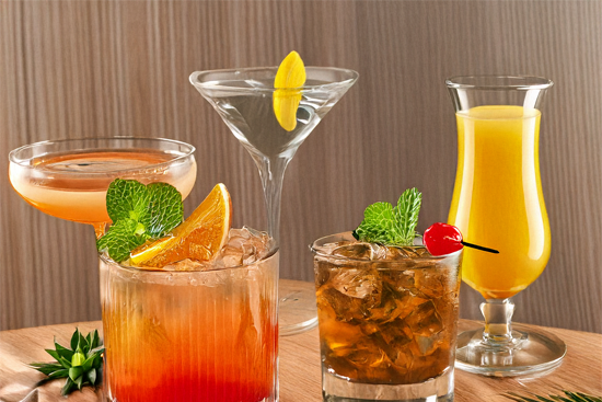 Assortiment de cocktails colorés servis dans différents verres avec fruits et glace.