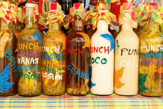 Plusieurs bouteilles de punch artisanal disposées côte à côte sur une nappe à carreaux créole. Chaque bouteille est décorée d’une étiquette colorée peinte à la main indiquant les saveurs — banane, mangue, passion, coco, café — et fermée par un bouchon recouvert d’un tissu coloré noué avec de la ficelle.