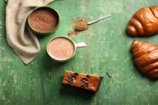 Tasse de chocolat chaud avec croissants et brioche au chocolat sur table en bois vert.