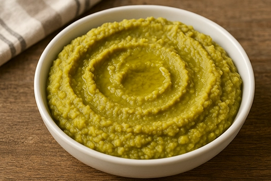Purée de pois cassés, appelée aussi purée Saint-Germain, servie dans un bol blanc sur une table en bois rustique. La texture est onctueuse et épaisse, d’un vert doré, avec un léger filet d’huile d’olive en surface. L’image évoque une préparation maison simple et réconfortante, mise en valeur par une lumière naturelle douce.