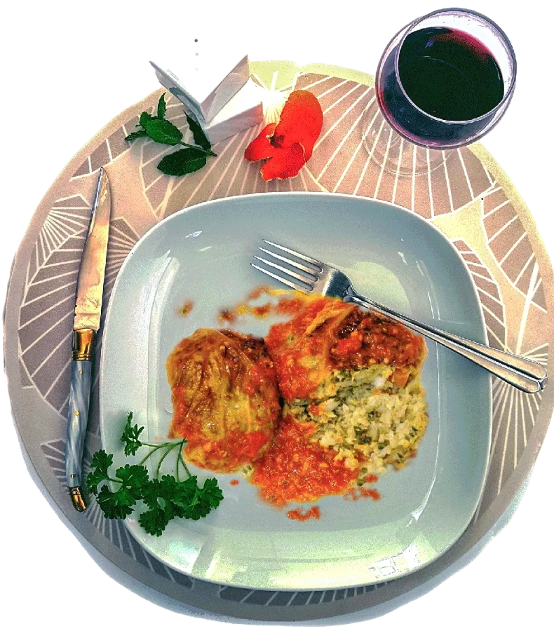 Deux capouns niçois à la sauce tomate, dont un coupé montrant une farce au riz, servis dans une assiette blanche avec persil, couverts et verre de vin rouge.