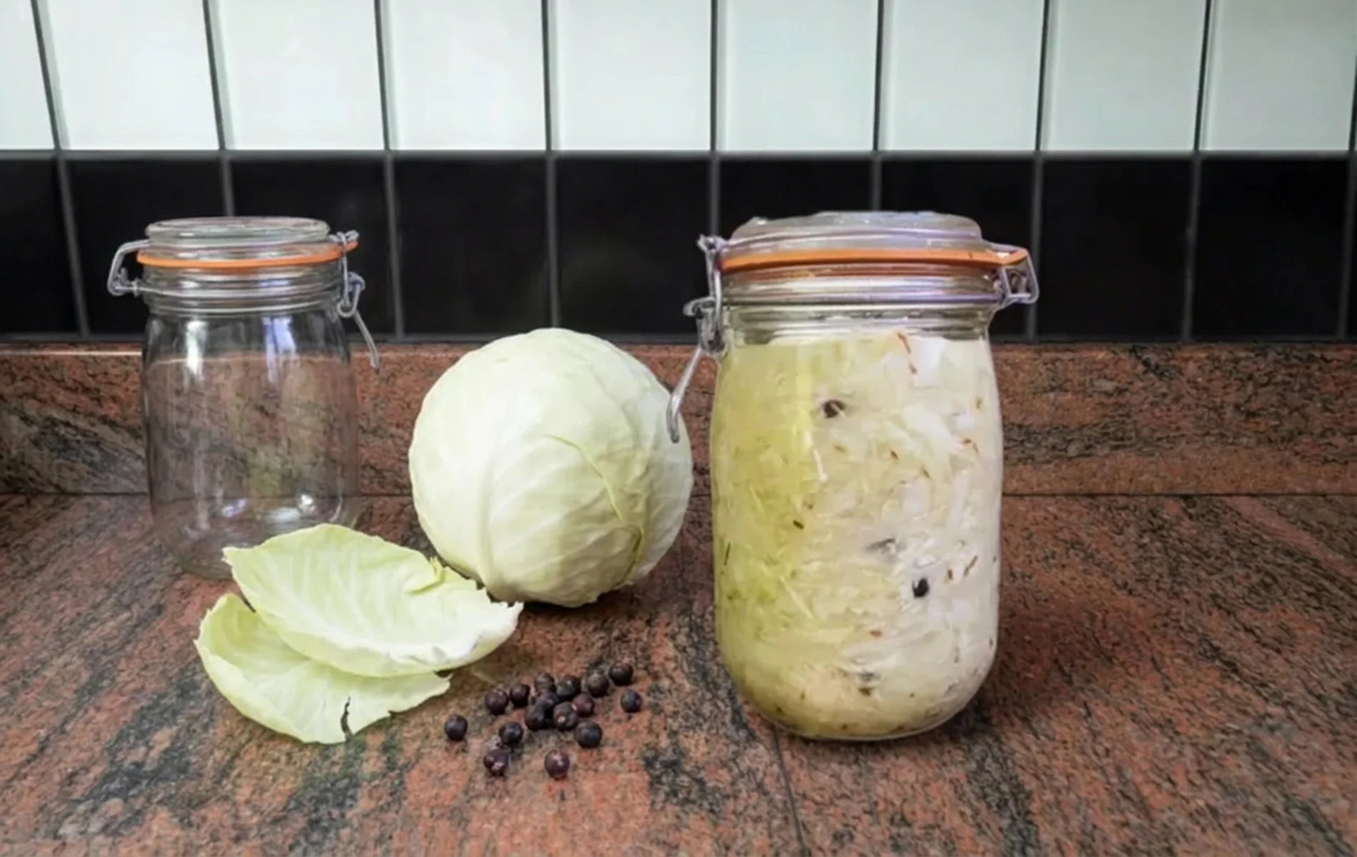 Chou blanc, baies de genièvre et bocal de choucroute crue en fermentation à côté d’un bocal vide.
