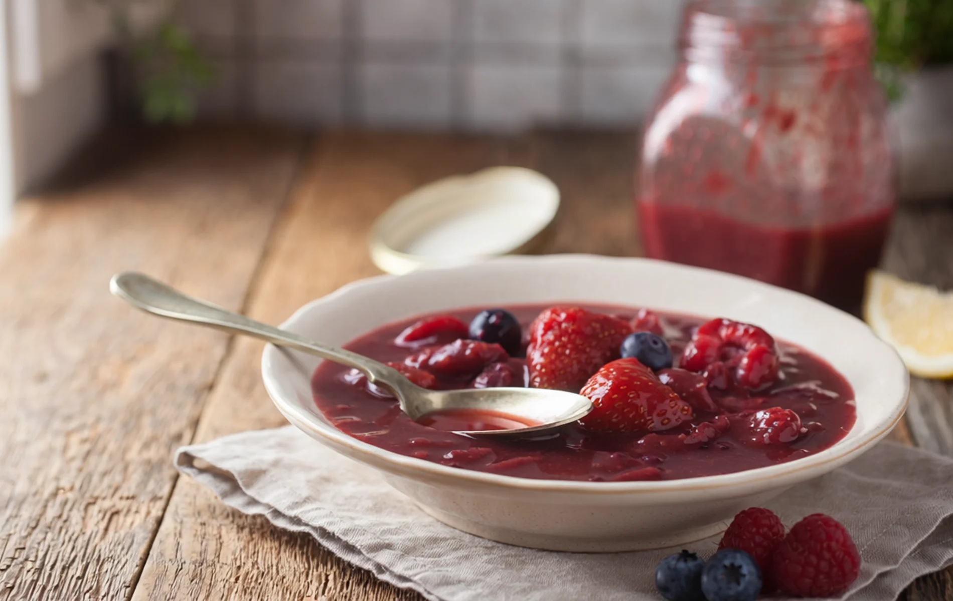 Bol de compotée de fruits rouges avec fraises et myrtilles entières, servi avec une cuillère sur une table en bois rustique.