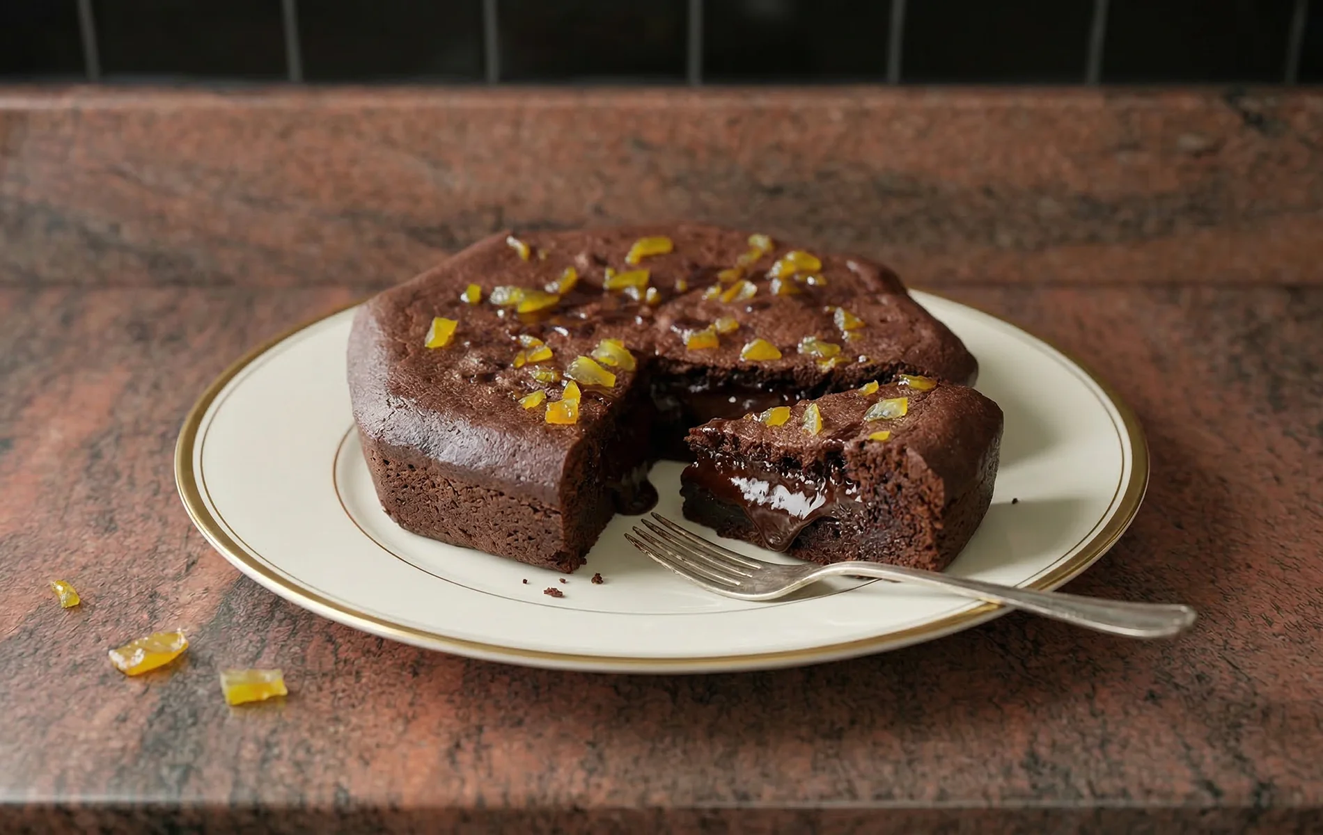 Gâteau mi-cuit au chocolat à la texture fondante, présenté sur une assiette, décoré d’écorces de yuzu, avec une part découpée laissant apparaître le cœur coulant.
