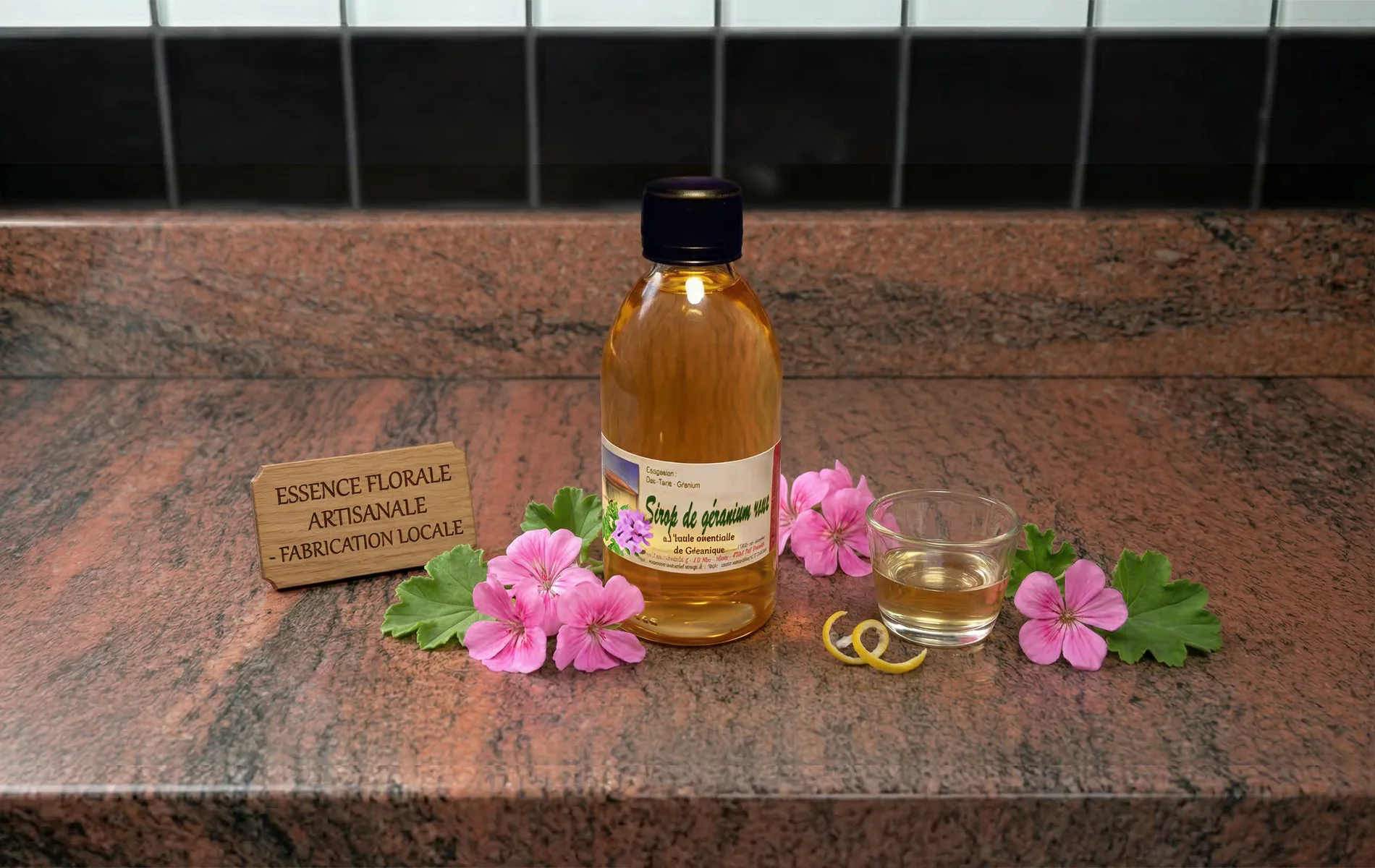 Bouteille de sirop de g&eacute;ranium avec fleurs fra&icirc;ches et verre de d&eacute;gustation