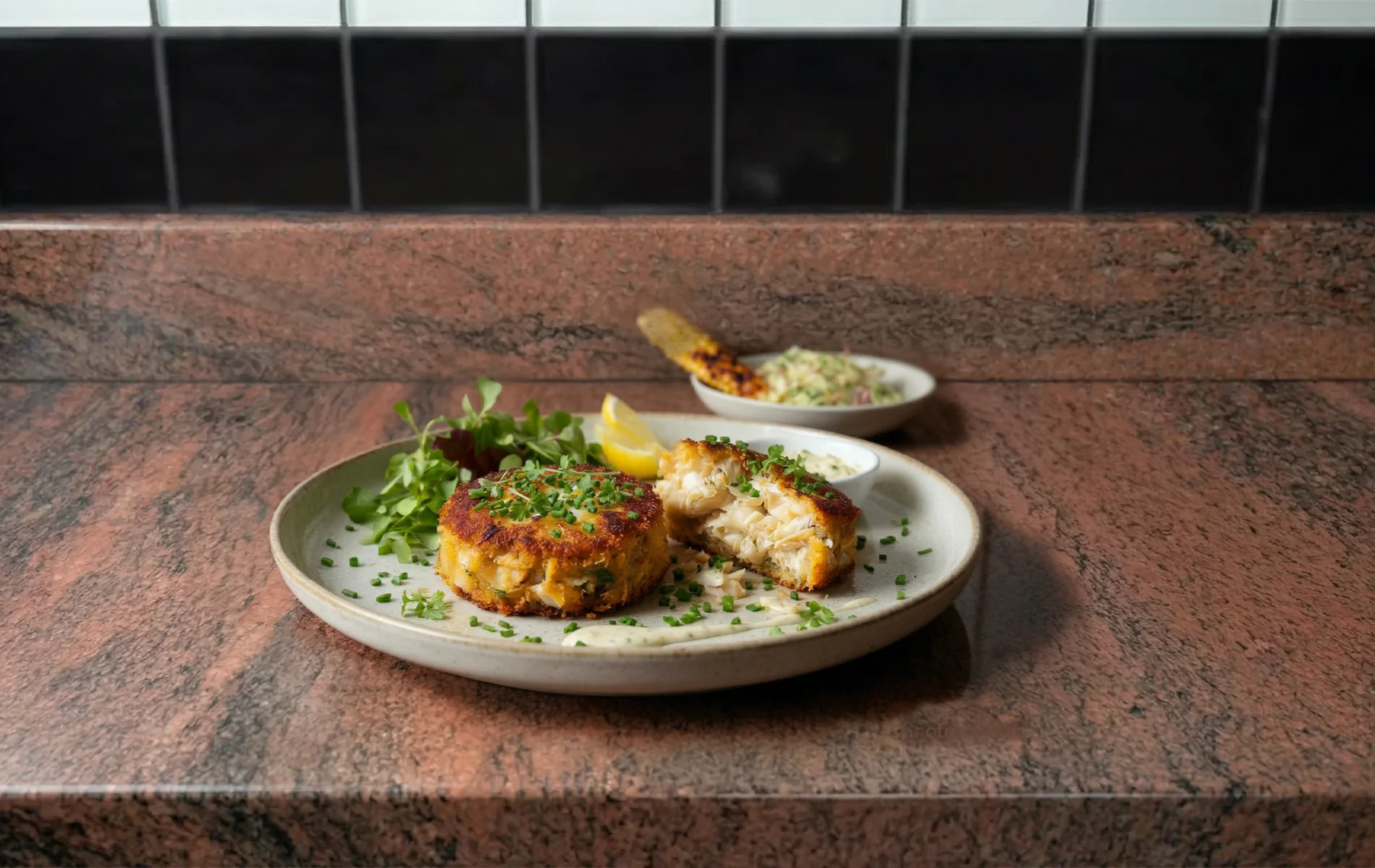 Galettes de crabe du Maryland dorées et croustillantes, avec chair de crabe en gros morceaux visible à cœur, servies avec salade, citron, sauce, coleslaw et maïs grillé.