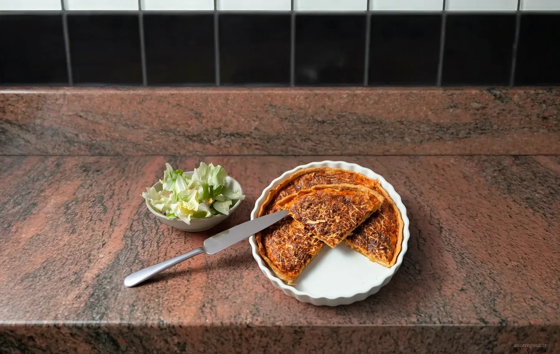 Quiche au surimi coup&eacute;e en parts, servie dans un moule blanc avec salade verte et couteau &agrave; c&ocirc;t&eacute;..