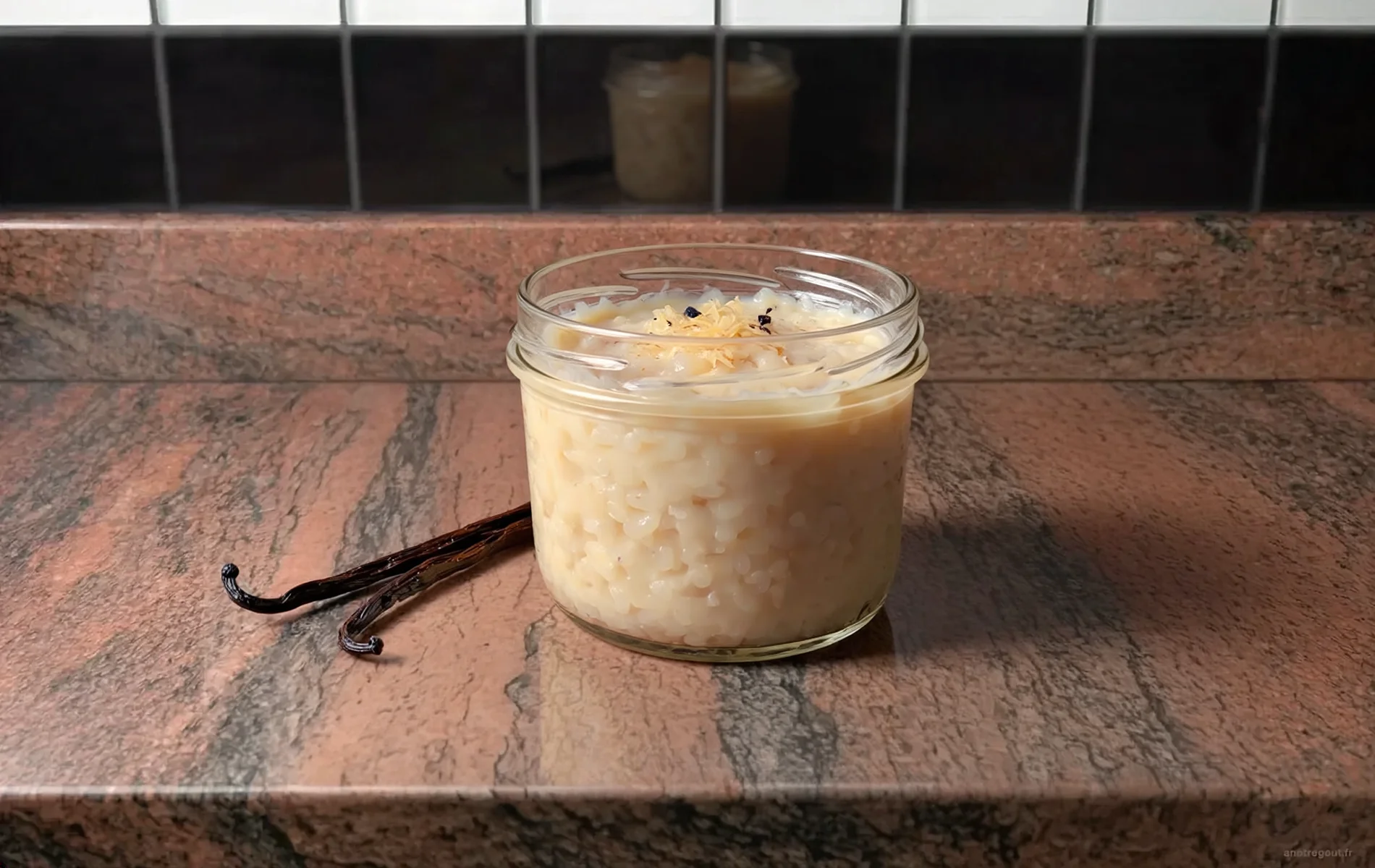 Pot en verre rempli d'un riz au lait &agrave; la vanille cr&eacute;meux, garni de quelques graines de vanille, accompagn&eacute; de deux gousses de vanille sur un plan de travail.
