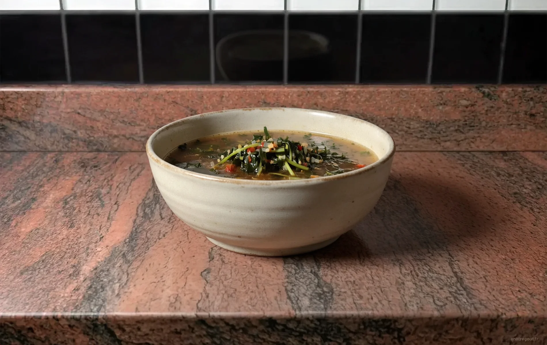 Bouillon de brèdes de La Réunion servi dans un bol en céramique, avec des feuilles de cresson, des oignons et des morceaux de tomate dans un bouillon clair.